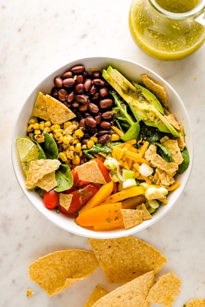 White bowl with the ingredients for a black bean taco salad with cilantro lime dressing.