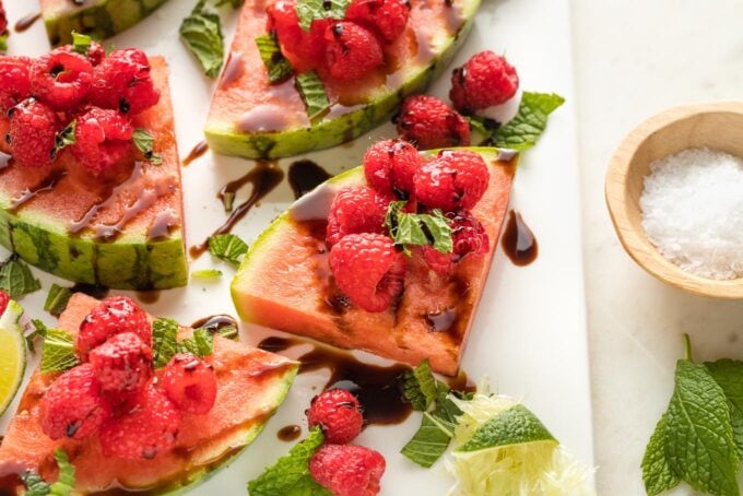 Close-up of a watermelon wedge served with raspberries, mint, lime, sea salt, and balsamic glaze.