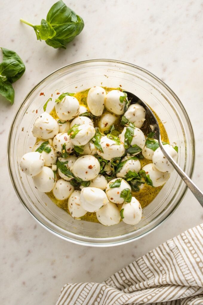 Mozzarella balls and olive oil mixture stirred together with a spoon.