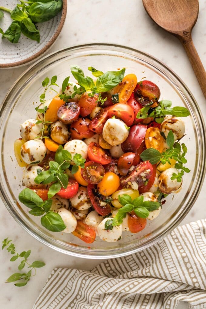 Bowl of marinated mozzarella balls served with cherry tomatoes and herbs as a salad.