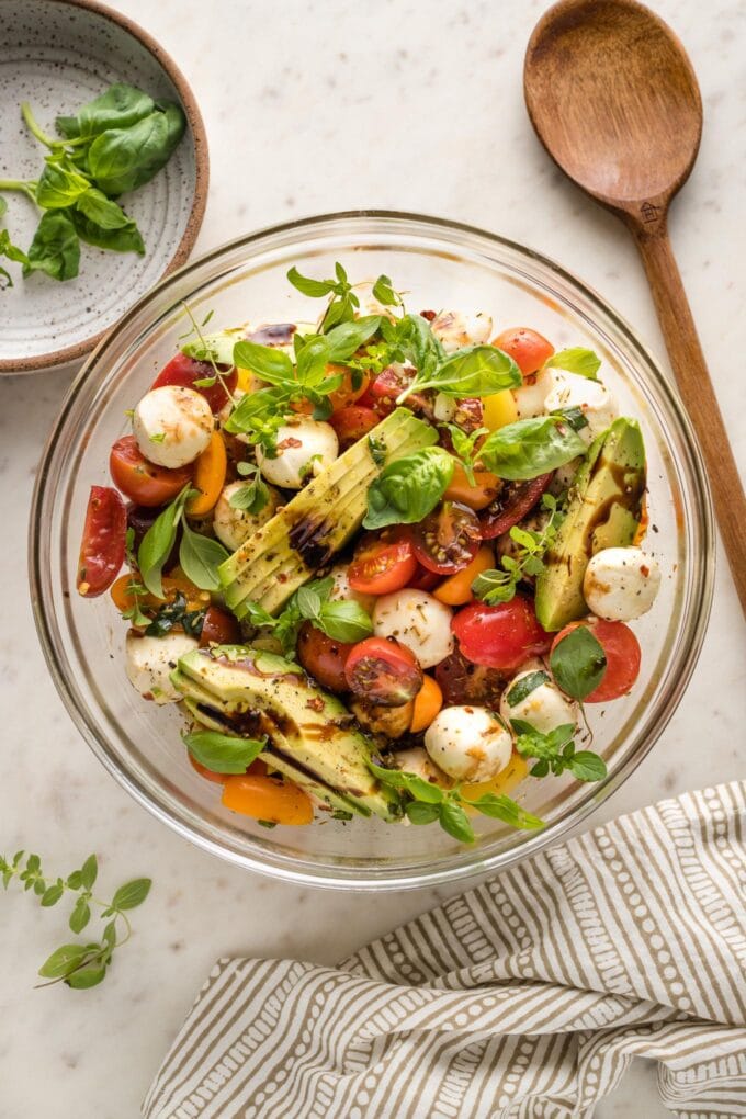 Bowl of marinated mozzarella balls served with cherry tomatoes and sliced avocado.