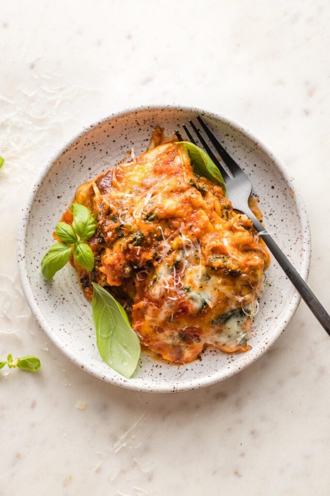 Baked ravioli served on a small speckled white plate with a garnish of fresh basil.