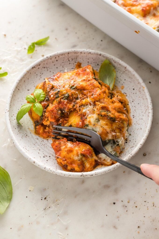 A fork digging into a plate of baked ravioli.