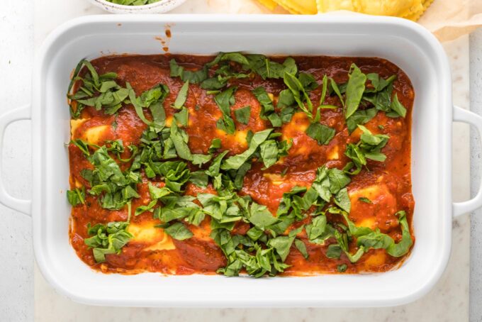 More sauce and spinach sprinkled on top of ravioli.