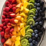 White platter filled with cut fruit arranged in a rainbow pattern.