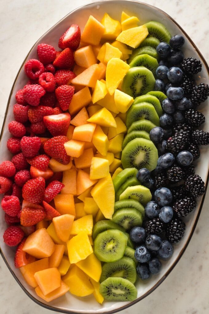 White platter filled with cut fruit arranged in a rainbow pattern.