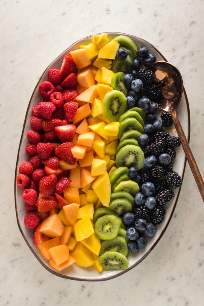 White platter filled with cut fruit arranged in a rainbow pattern.