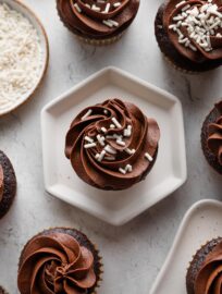 Overhead image of a chocolate cupcake with white sprinkles resting on a hexagonal plate.