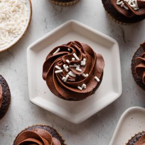 Overhead image of a chocolate cupcake with white sprinkles resting on a hexagonal plate.