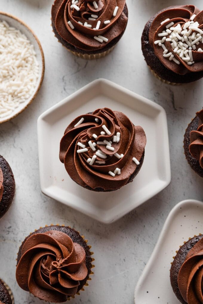 Overhead image of a chocolate cupcake with white sprinkles resting on a hexagonal plate.