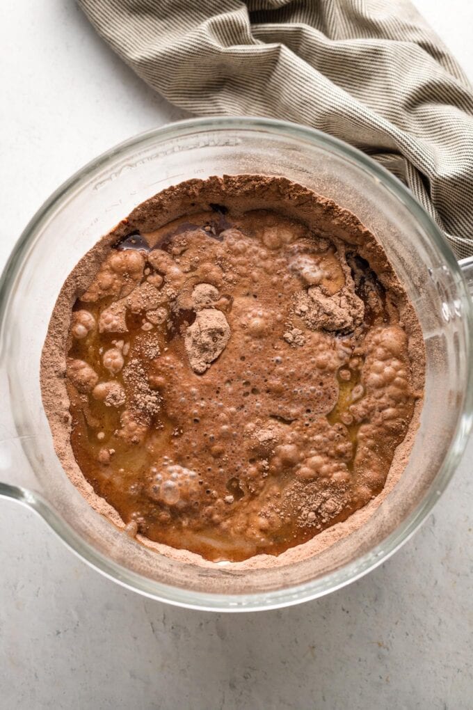 Dry and liquid ingredients for chocolate buttermilk cupcakes combined in a clear glass mixing bowl, but not yet blended together.