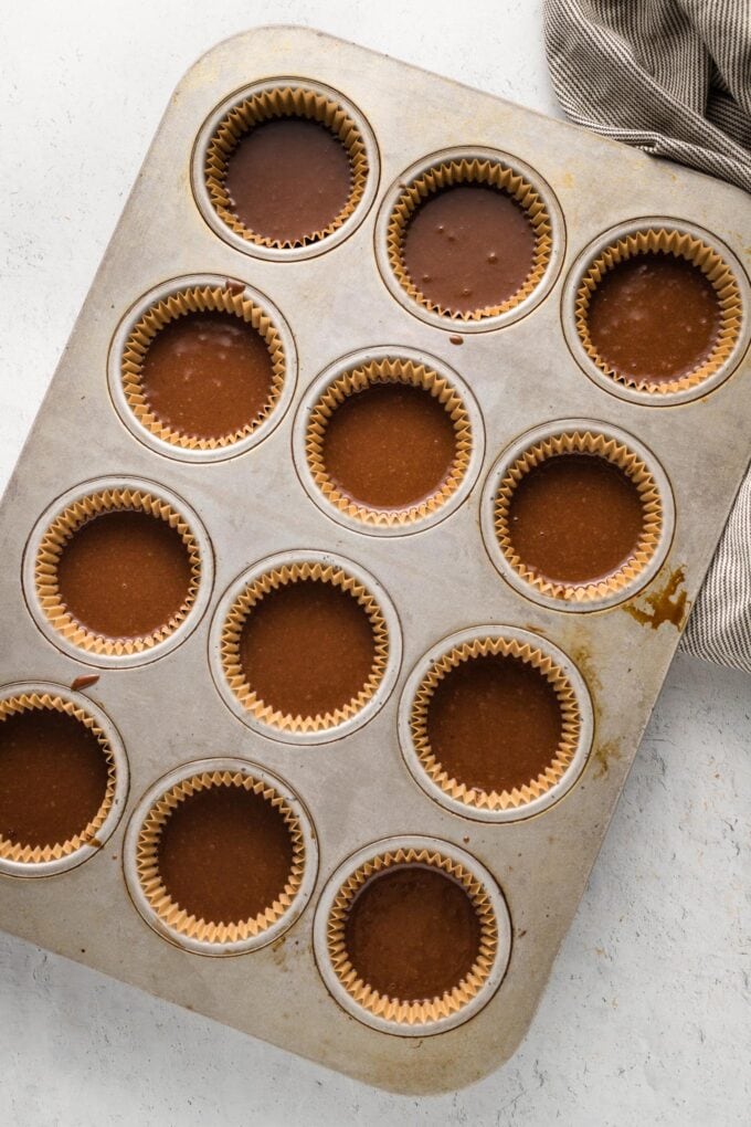 Cupcake batter divided among cupcake liners in a muffin tin, ready to bake.