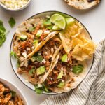 Small plate holding three shredded chicken tacos.