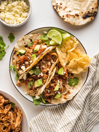 Small plate holding three shredded chicken tacos.