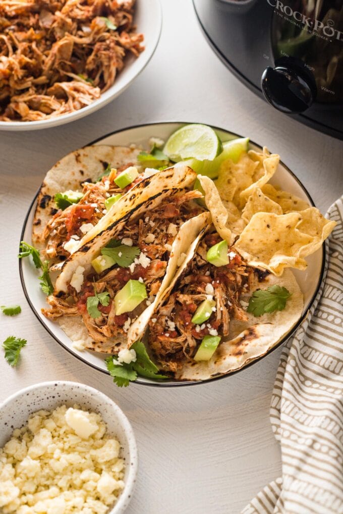Shredded chicken tacos made in the crockpot, served on a small plate with lime wedges and tortilla chips.