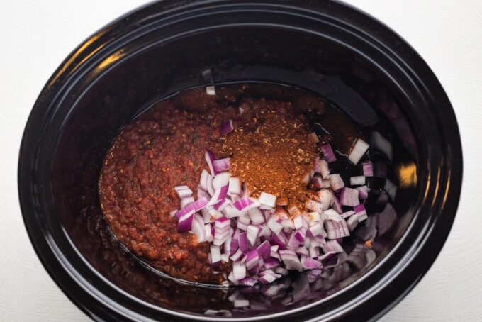 Salsa, taco seasoning, and red onion in the bottom of a slow cooker.