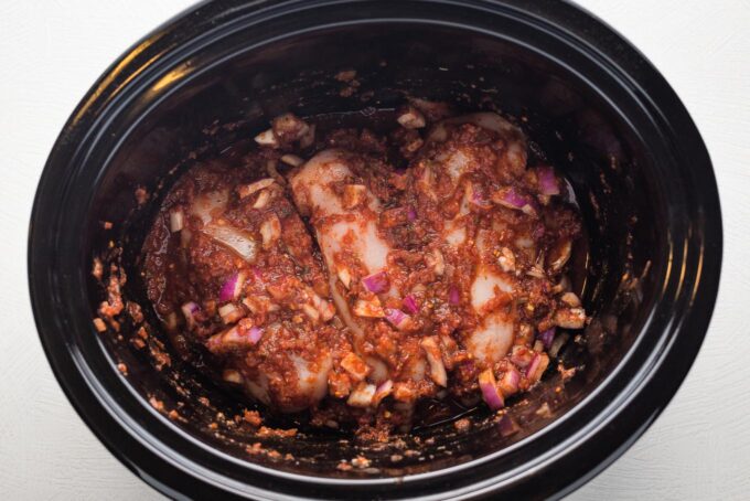 Chicken nestled into salsa mixture in slow cooker.