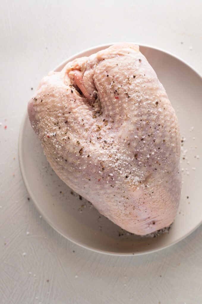 Turkey breast on a plate, seasoned generously with salt and pepper.