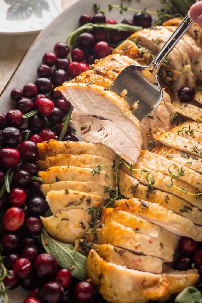 Close up of a serving fork piercing a tender, juicy piece of turkey breast.
