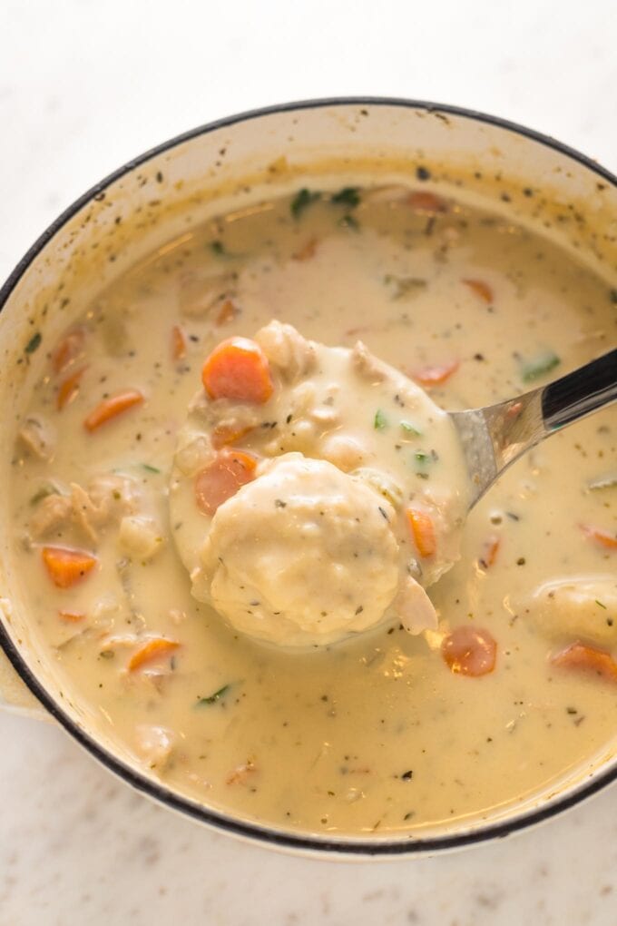 Finished turkey and dumplings soup in Dutch oven, garnished with parsley and being served with a ladle.