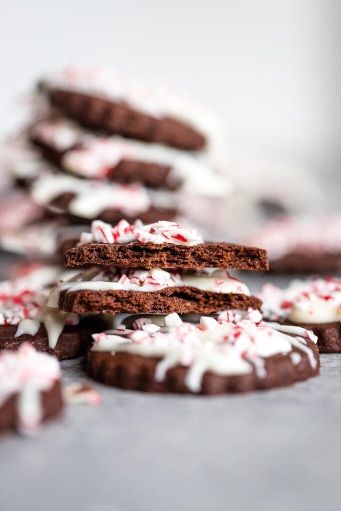 Close up of a peppermint bark cookie, broken in half to show the tender chocolate sugar cookie inside.