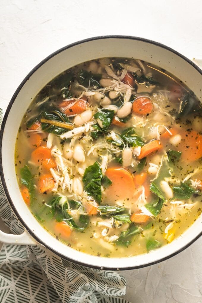 White bean chicken soup with rainbow chard, carrots, and onions, simmering in a Dutch oven ready to serve.