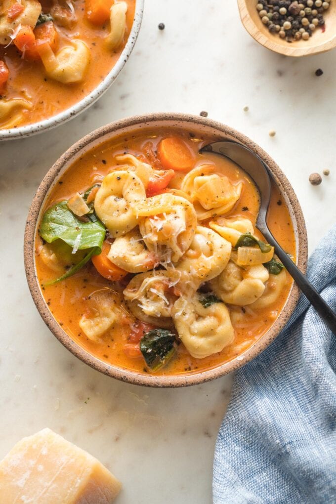 Bowl of soup surrounded by extra pepper and Parmesan.