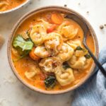 Small bowl of creamy tomato tortellini soup served with black pepper and fresh grated Parmesan.