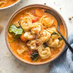 Small bowl of creamy tomato tortellini soup served with black pepper and fresh grated Parmesan.