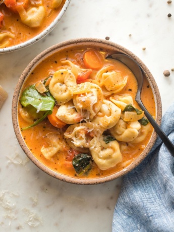 Small bowl of creamy tomato tortellini soup served with black pepper and fresh grated Parmesan.