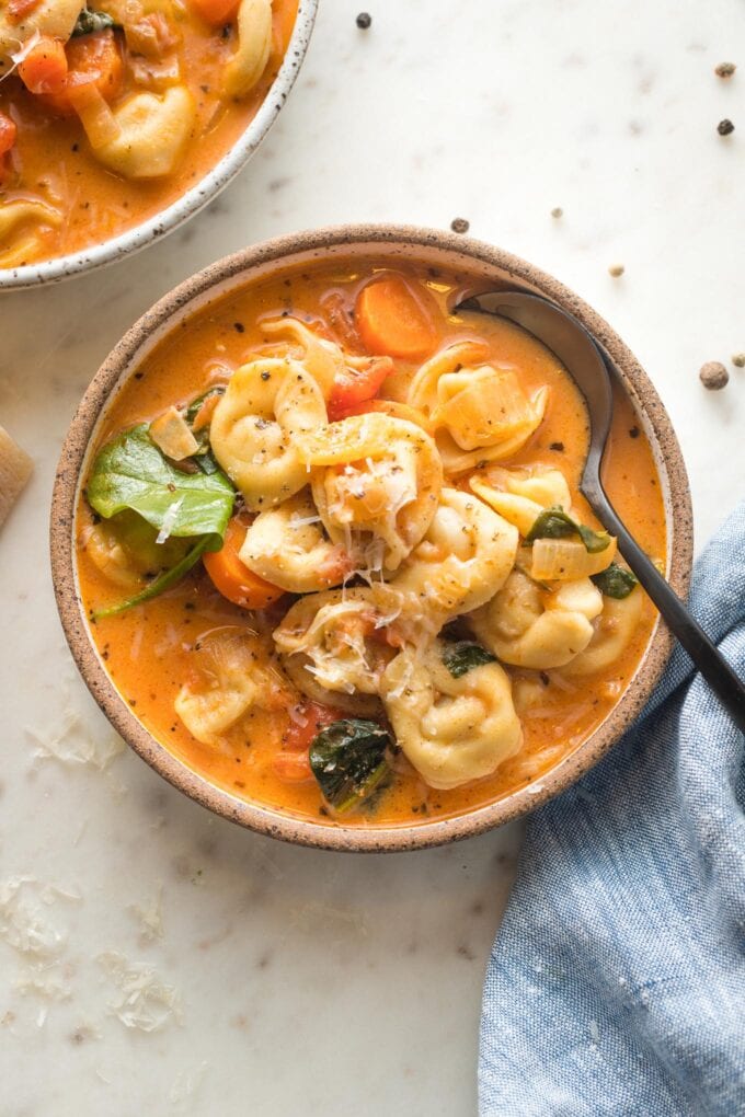 Small bowl of creamy tomato tortellini soup served with black pepper and fresh grated Parmesan.