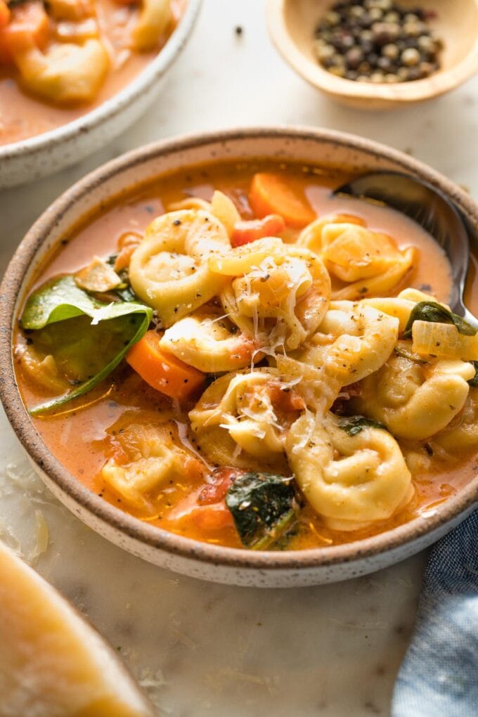 Side view of a spoon lifting a bite of creamy tomato tortellini soup.
