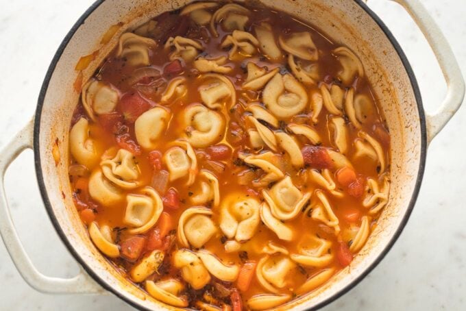 Broth bubbling with tortellini cooking inside of Dutch oven.