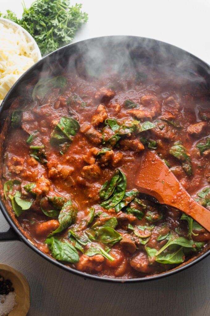 Tomato sauce with ground turkey, seasonings, and baby spinach cooking in a skillet.