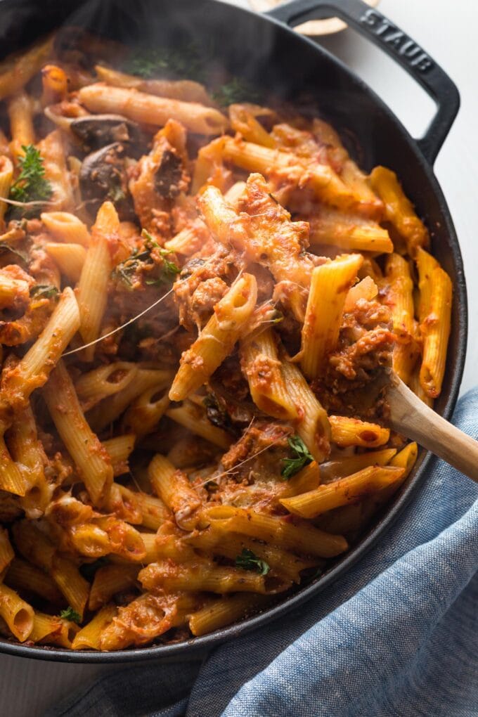 Melted cheese stretching as a serving of pasta is scooped from a large cast iron skillet.