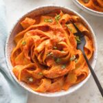 Small bowl of creamy roasted red pepper pasta with Parmesan and red pepper flakes.