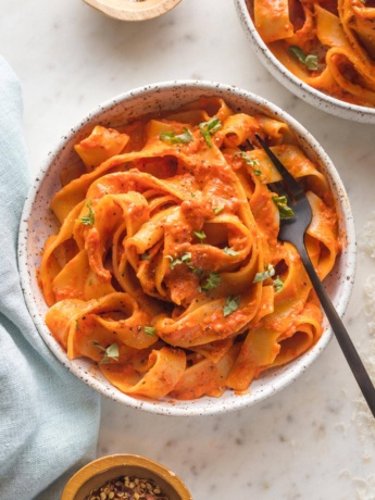 Small bowl of creamy roasted red pepper pasta with Parmesan and red pepper flakes.