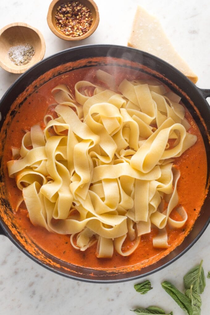 Al dente pappardelle noodles added to a large skillet with creamy roasted red pepper sauce.