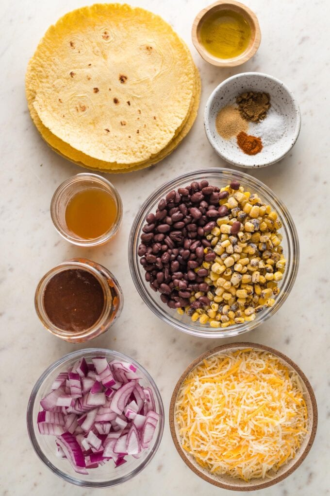 Prep bowls with black beans, corn, shredded cheese, red onion, enchilada sauce, broth, and seasonings.