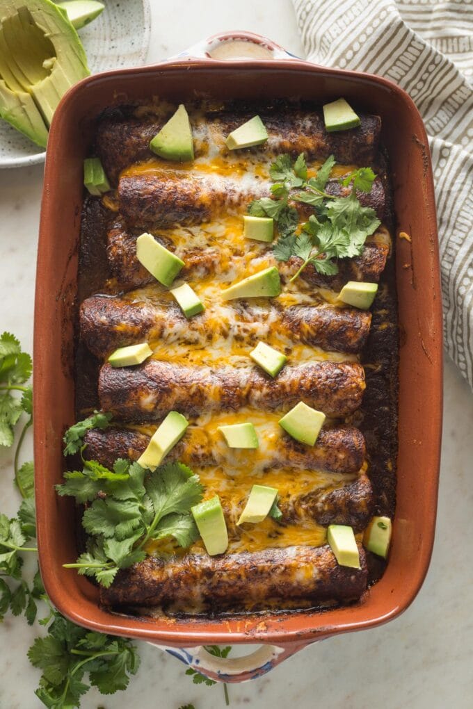 Chopped avocado and cilantro added to black bean enchiladas for garnish.