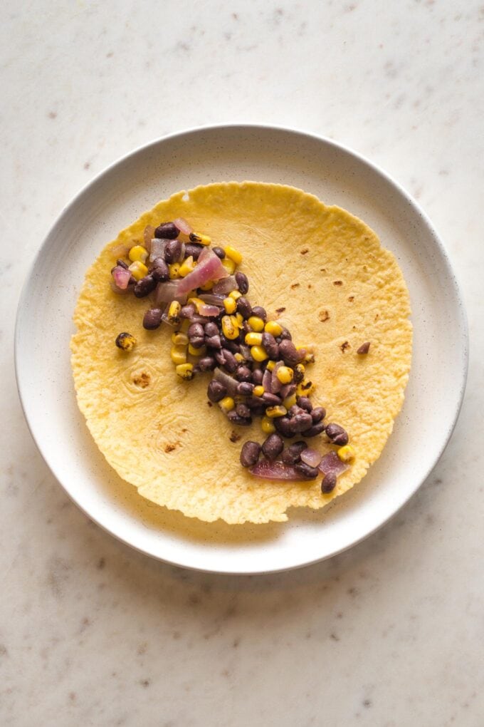 Plate with an open tortilla filled with about 3 tablespoons of black beans and corn.