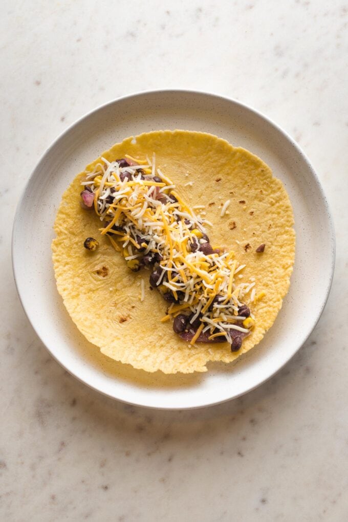 Cheese added to black bean and corn mixture in a tortilla.