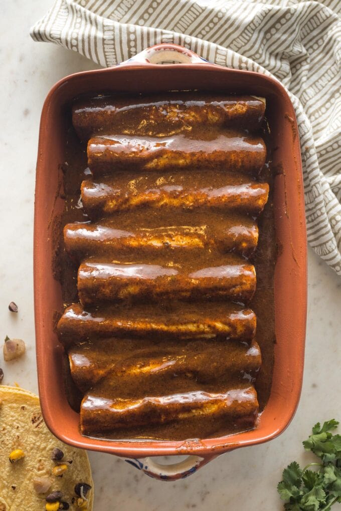 Enchilada sauce poured in an even layer over rolled up tortillas.