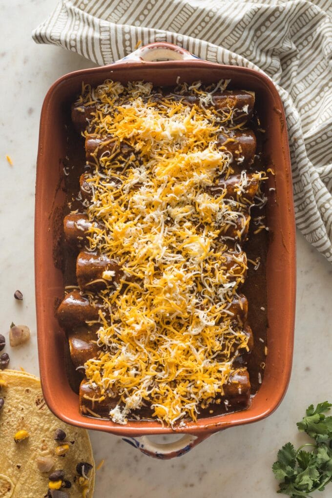 Cheese sprinkled on top of black bean and corn enchiladas, ready to bake.