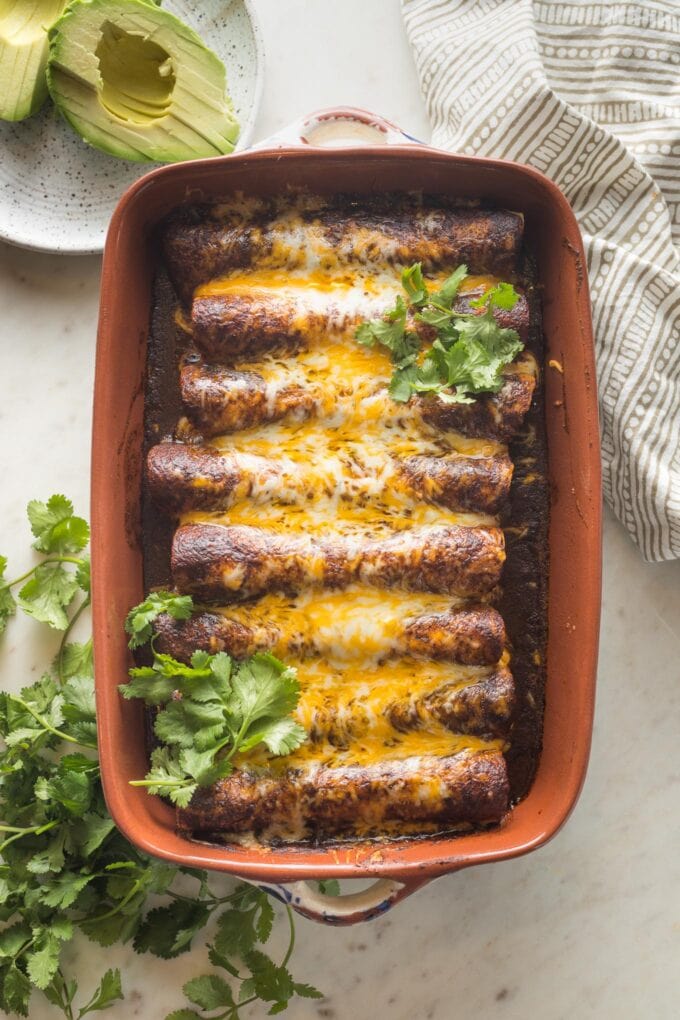 Brown ceramic baking dish filled with black bean and corn enchiladas fresh out of the oven.