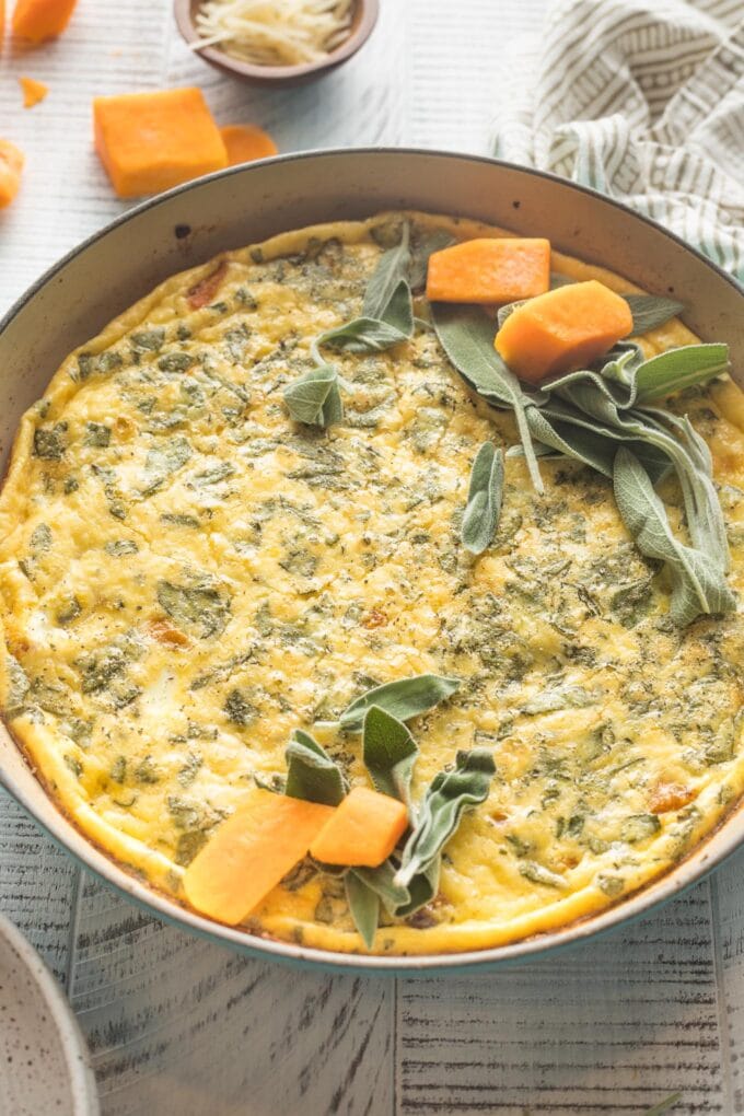 Frittata ready to slice, garnish with cubed butternut squash and fresh sage leaves.