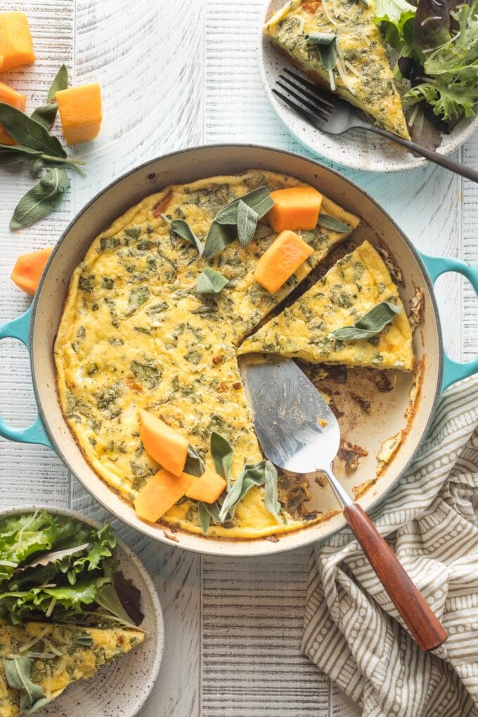 A butternut squash frittata with sage and red onion, sliced and being served from a cast iron skillet.