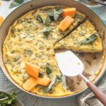 A butternut squash frittata with sage and red onion, sliced and being served from a cast iron skillet.