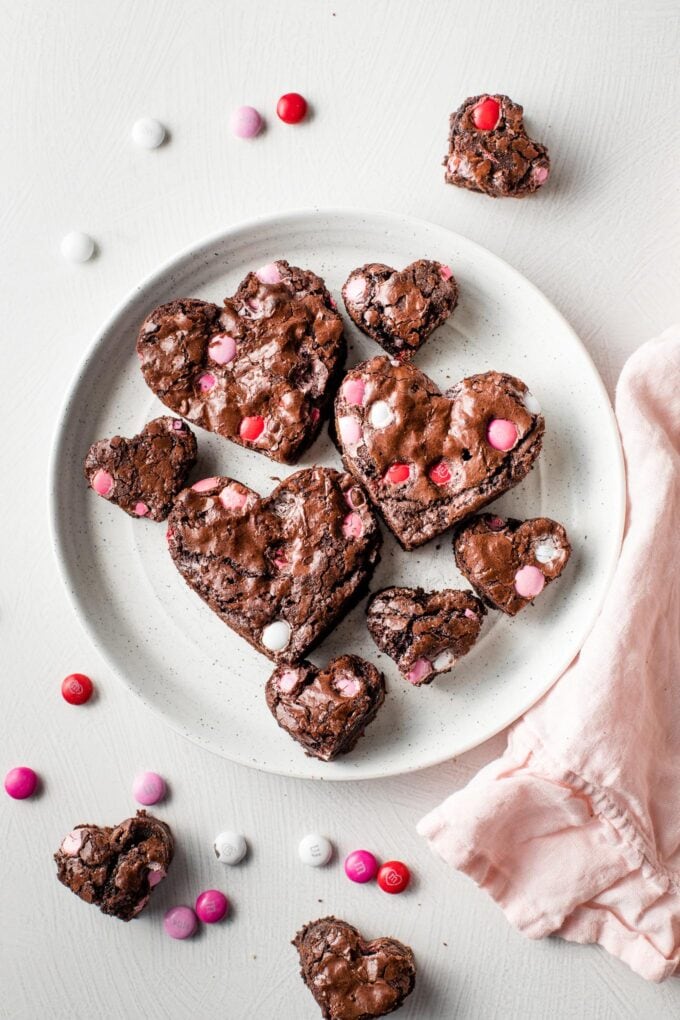 A small white plate holding heart shaped brownies pressed with pink, red, and white M&Ms.