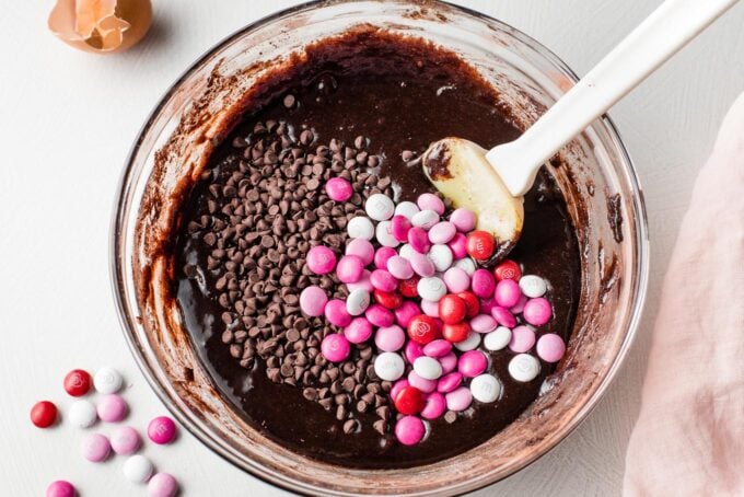 Chocolate chips and M&Ms sprinkled over a prep bowl of brownie batter.